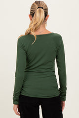 woman wearing a dark green long sleeve maternity top with ruching details at the sides