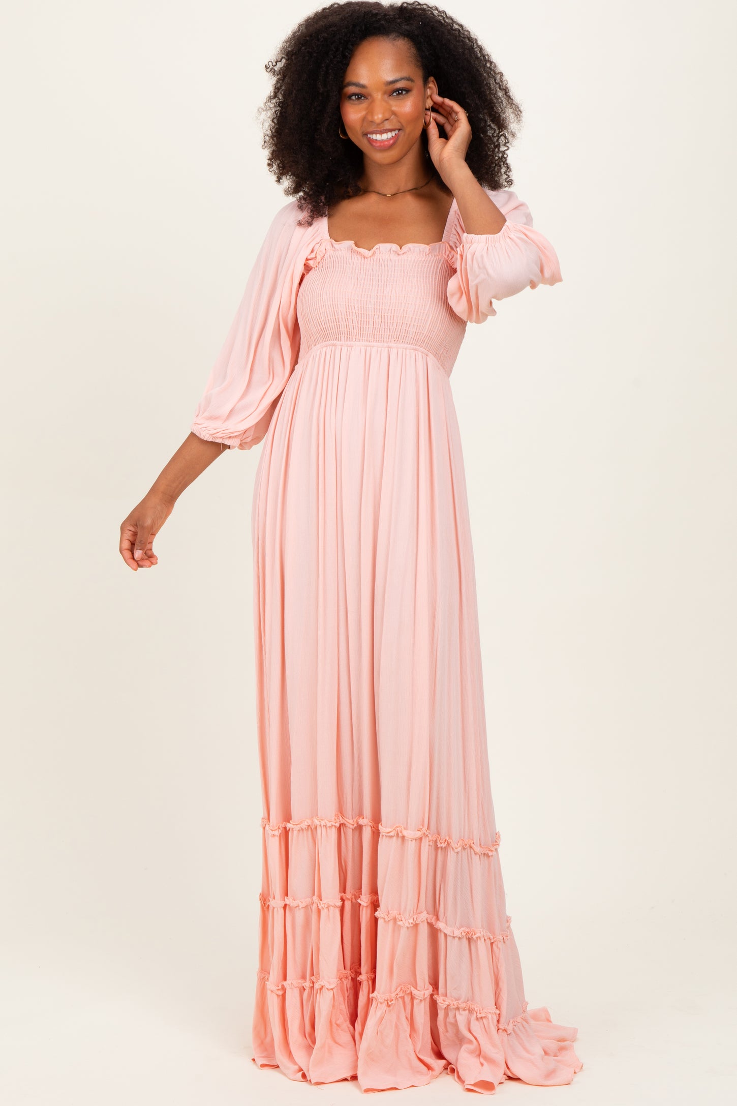 woman wearing a pink maxi dress with smocked bodice and puff sleeves, standing and smiling
