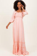 woman wearing a pink maxi dress with smocked bodice and puff sleeves, standing and smiling