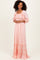 woman wearing a light pink maxi dress with smocked bodice and tiered skirt, standing against a light background