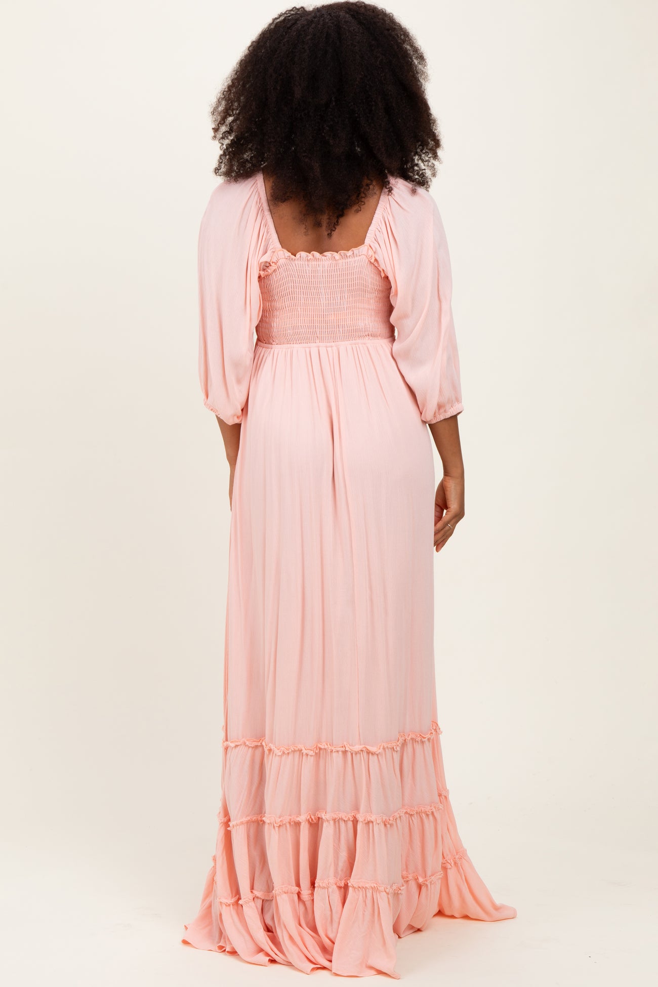 woman wearing a pastel pink maxi dress with smocked bodice and ruffled hem, viewed from the back