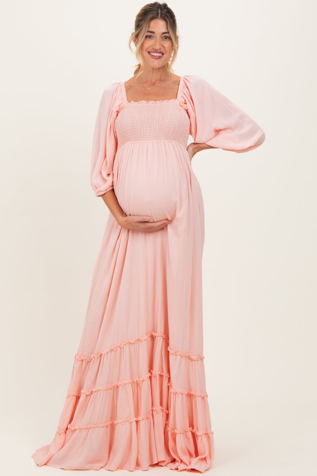 woman wearing a light pink maternity maxi dress with puff sleeves and ruffled hem, highlighting her baby bump