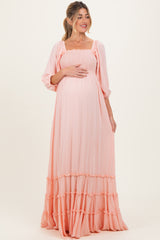 woman wearing a light peach maternity maxi dress with smocked bodice and tiered ruffle hem, holding her baby bump