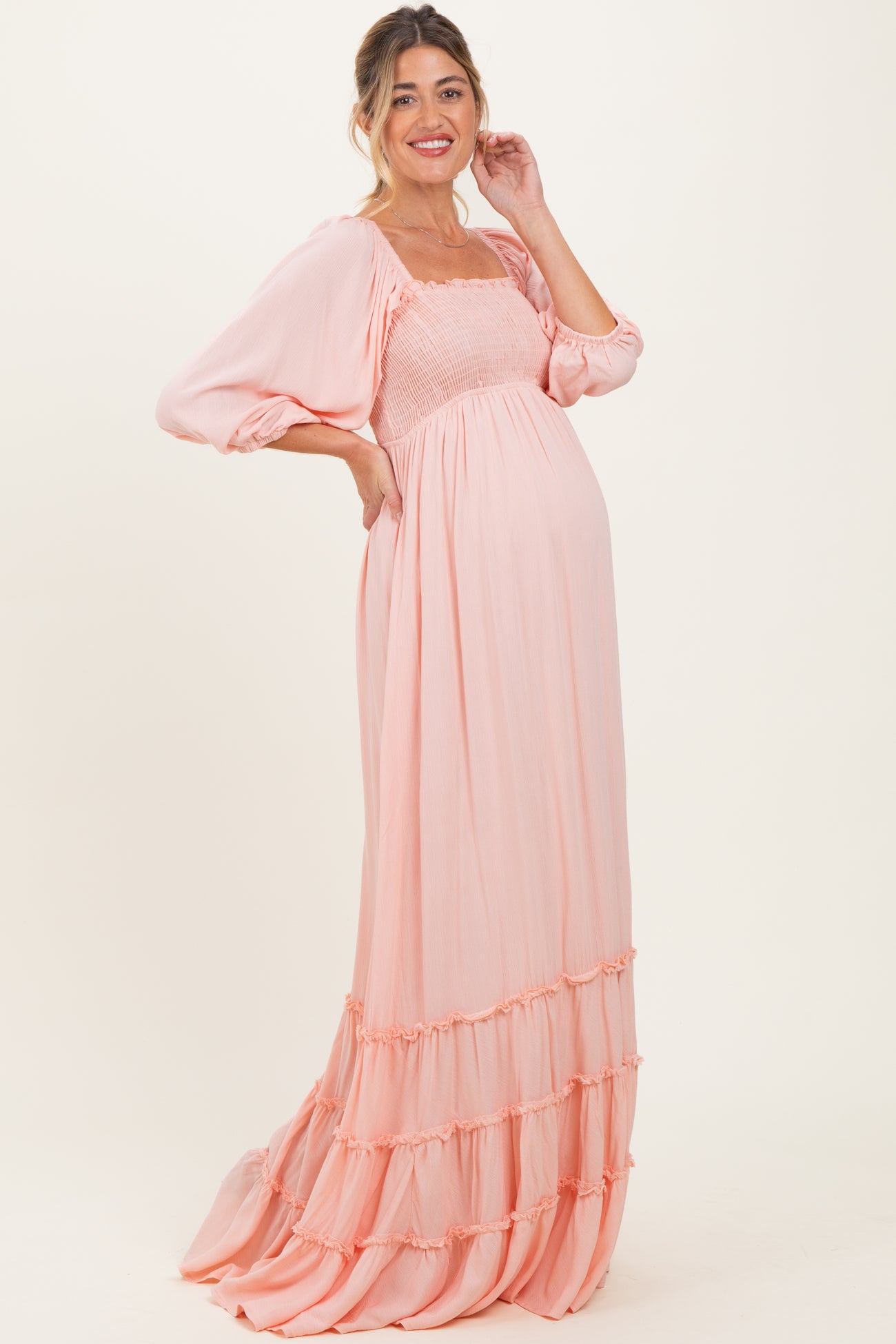 woman wearing a peach maternity gown with smocked bodice and ruffled hem, displaying her baby bump