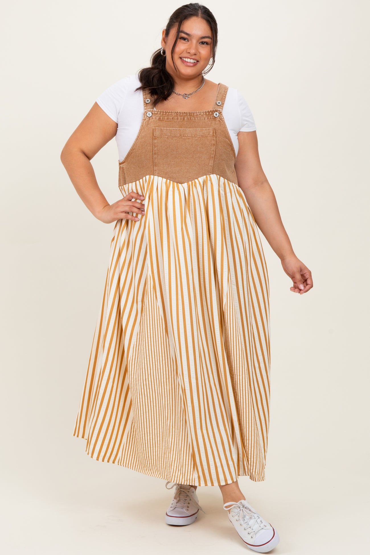woman wearing a plus size striped maxi dress with a tan and white color scheme and denim-style top portion