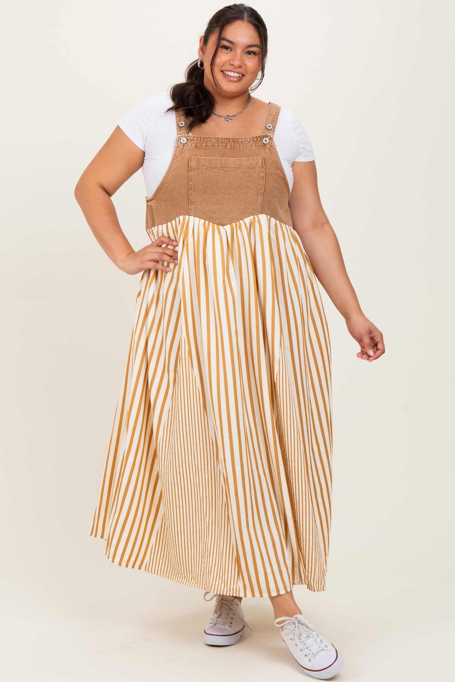 woman wearing a plus size striped maxi dress with a tan and white color scheme and denim-style top portion