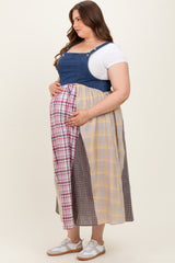 woman wearing a denim maternity plus jumpsuit dress with a colorful plaid skirt and holding her baby bump