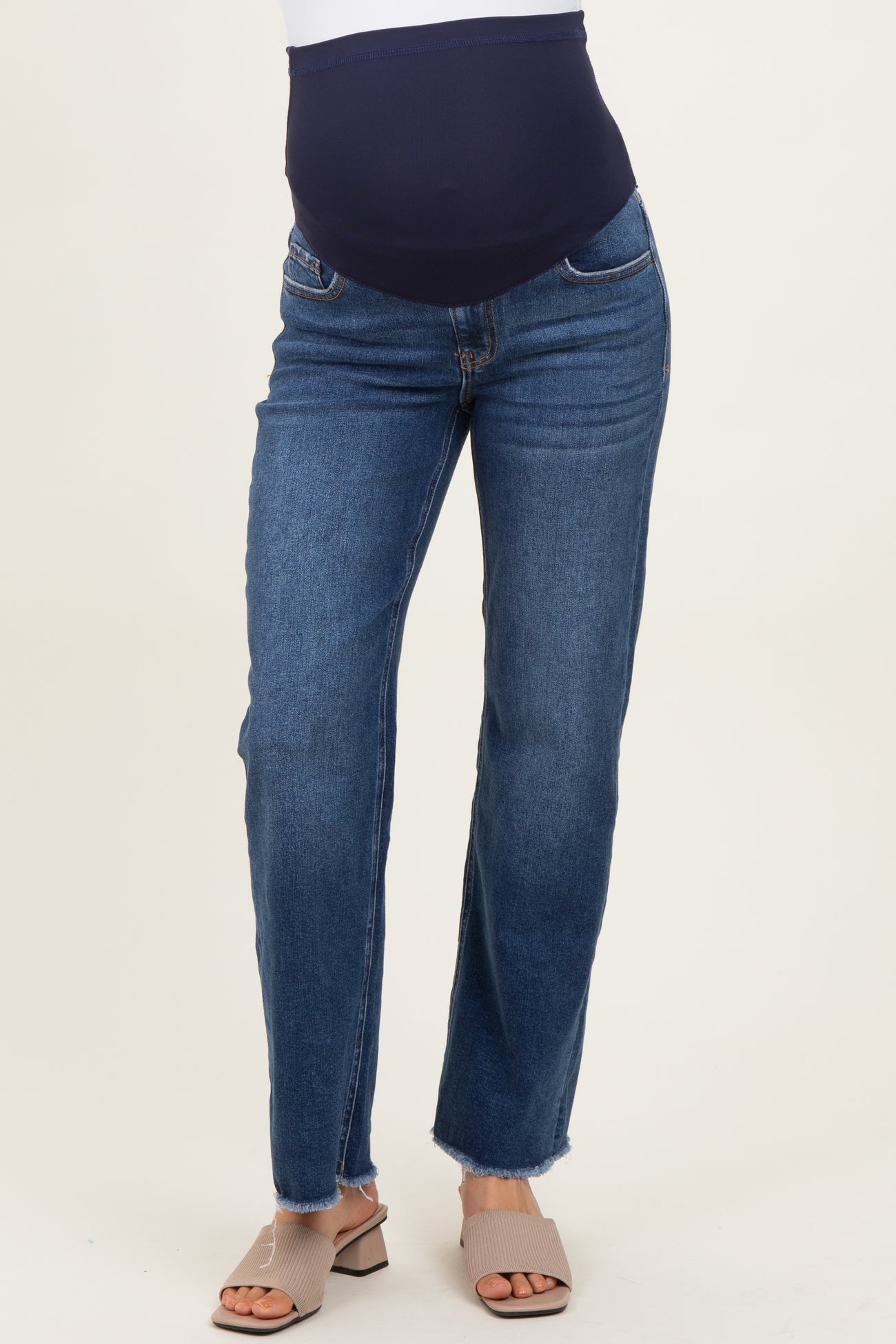 woman wearing dark blue maternity jeans with a supportive belly band and a frayed hem, paired with light beige sandals