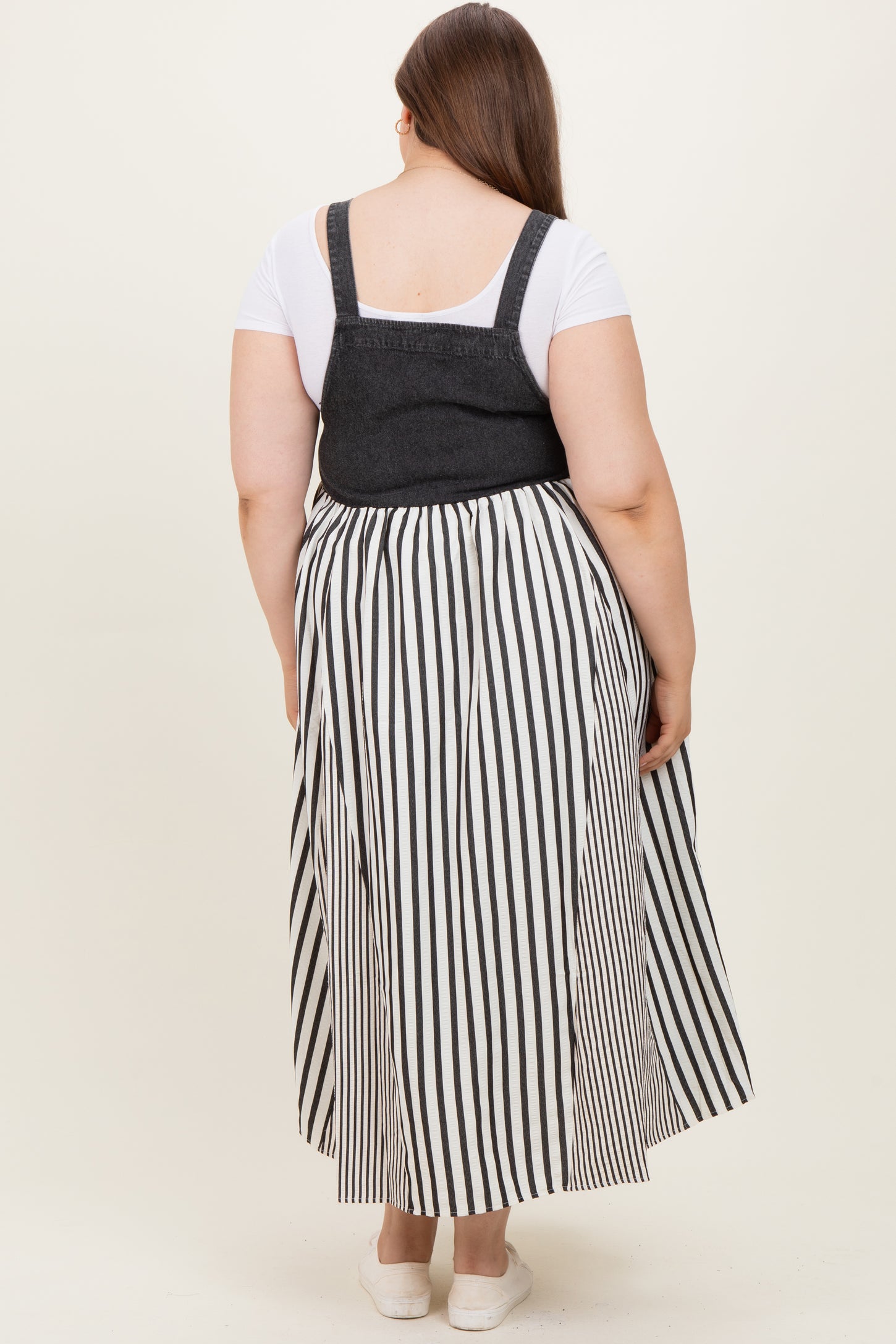 woman wearing a black and white striped maternity plus dress with a denim top and a flowy skirt, showing a baby bump