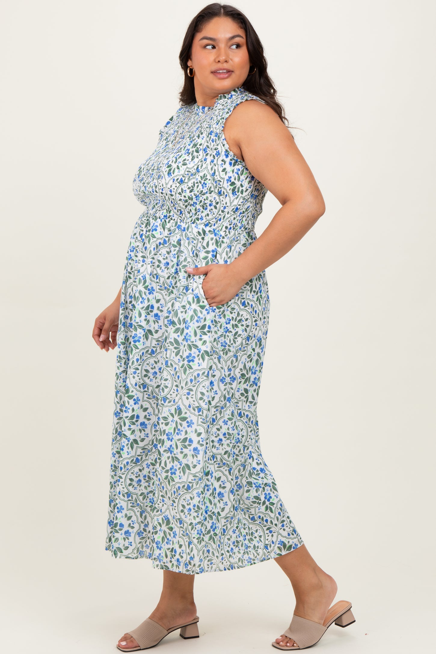 woman wearing a floral print plus size maxi dress with ruffle details and pockets, styled with light heels