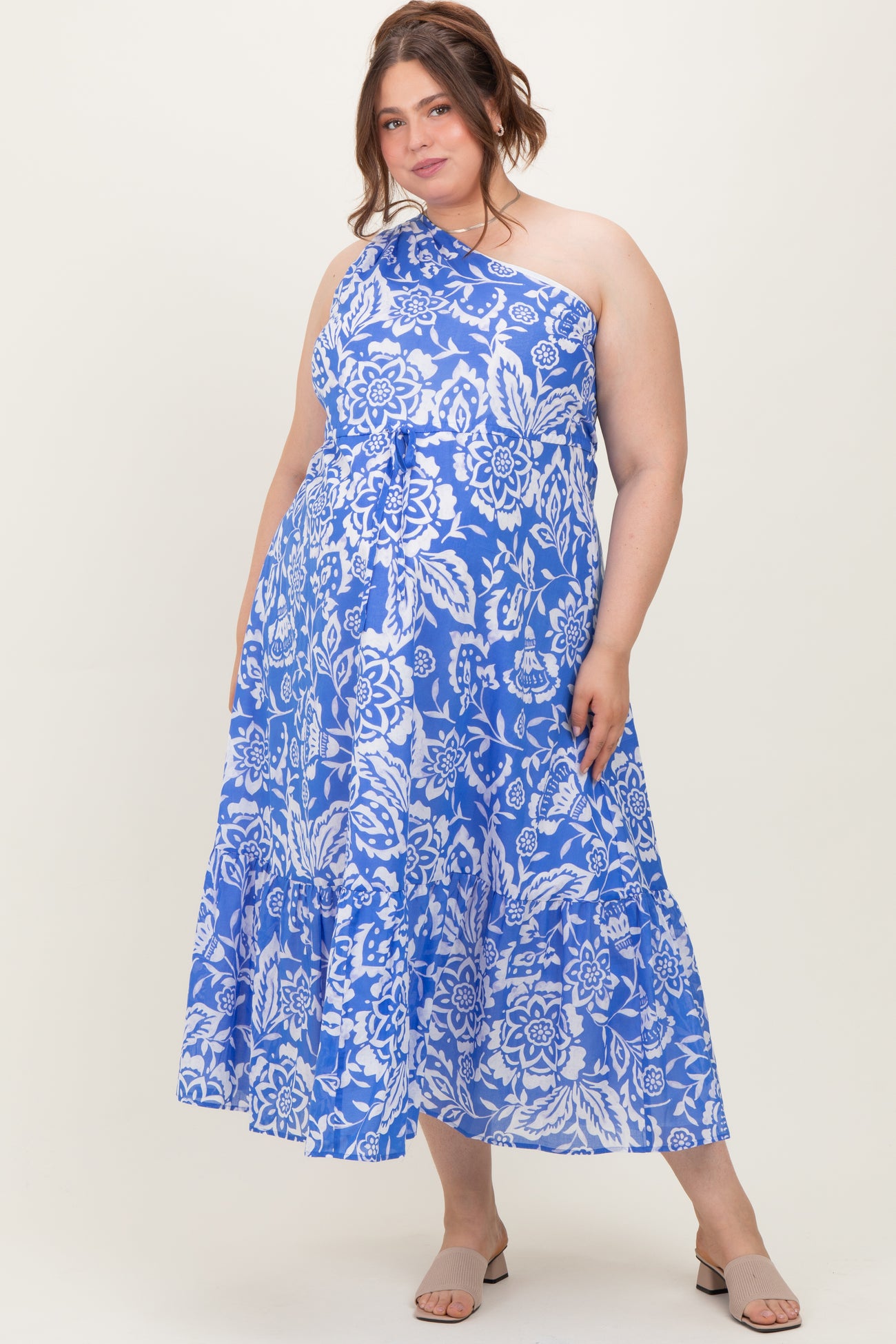 woman wearing a blue and white floral one-shoulder maternity plus dress with a tiered skirt and a flowing silhouette