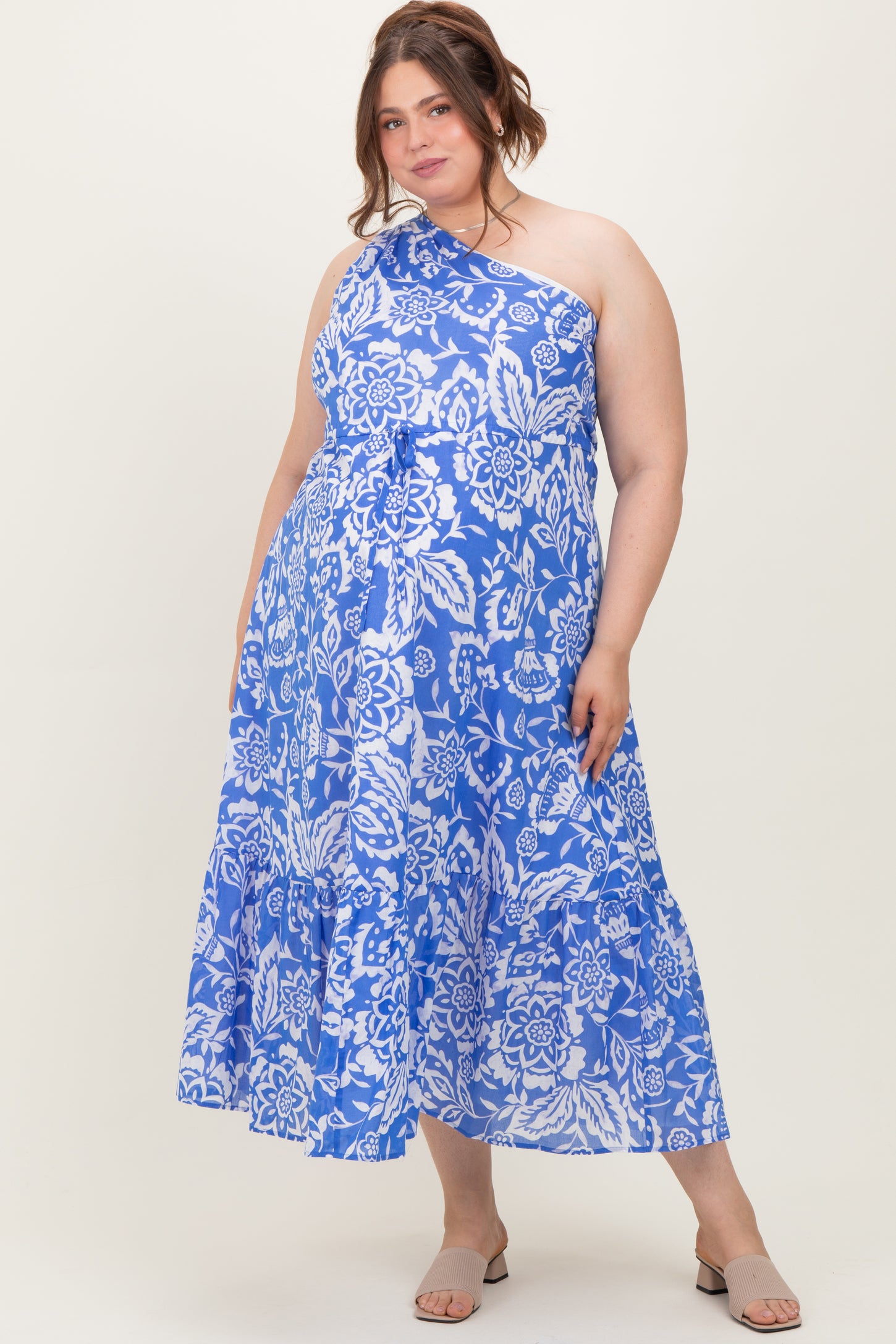 woman wearing a blue and white floral one-shoulder maternity plus dress with a tiered skirt and a flowing silhouette