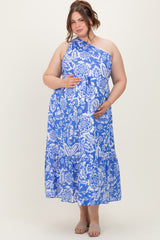 woman wearing a blue floral print one-shoulder maternity dress and holding her baby bump