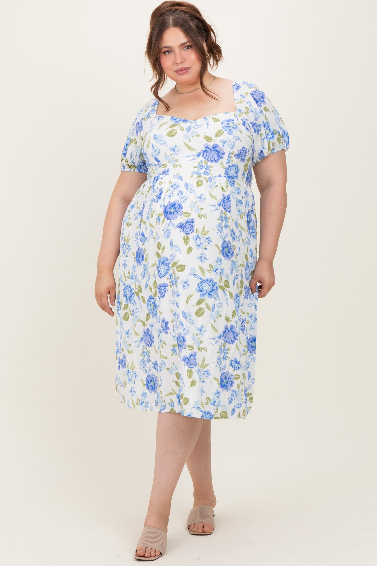 woman wearing a floral midi maternity dress in white, blue, and green with puff sleeves and a square neckline, showing her baby bump