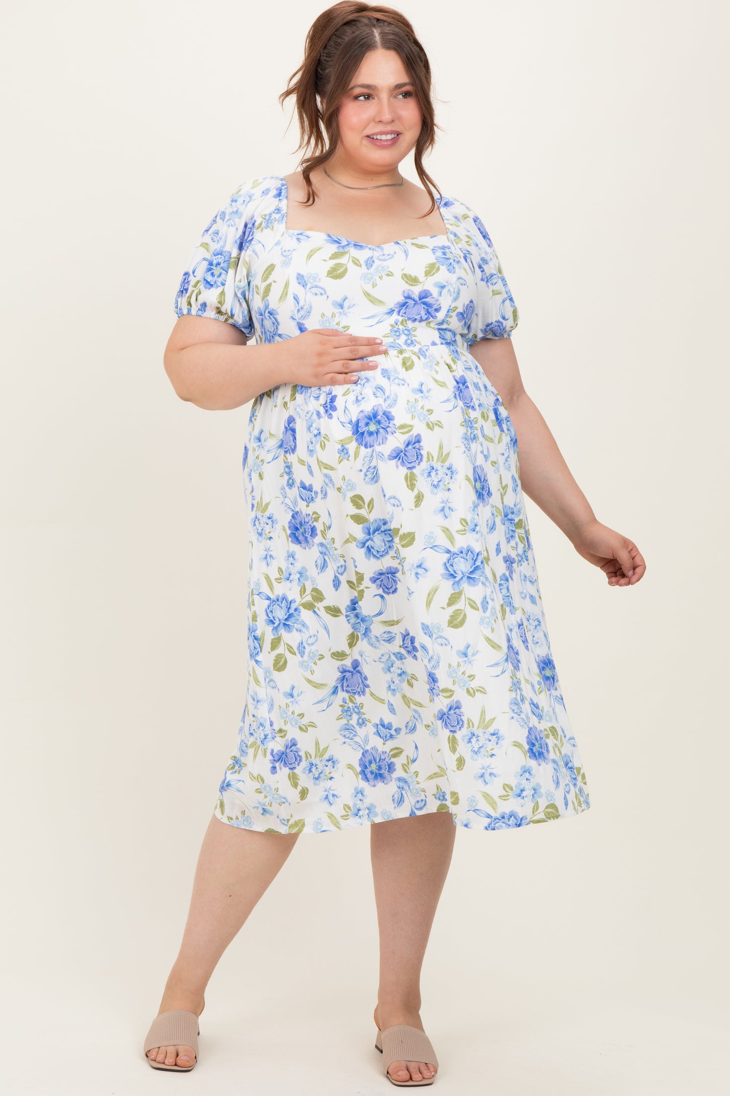 woman wearing a light blue and white floral maternity dress, holding her baby bump