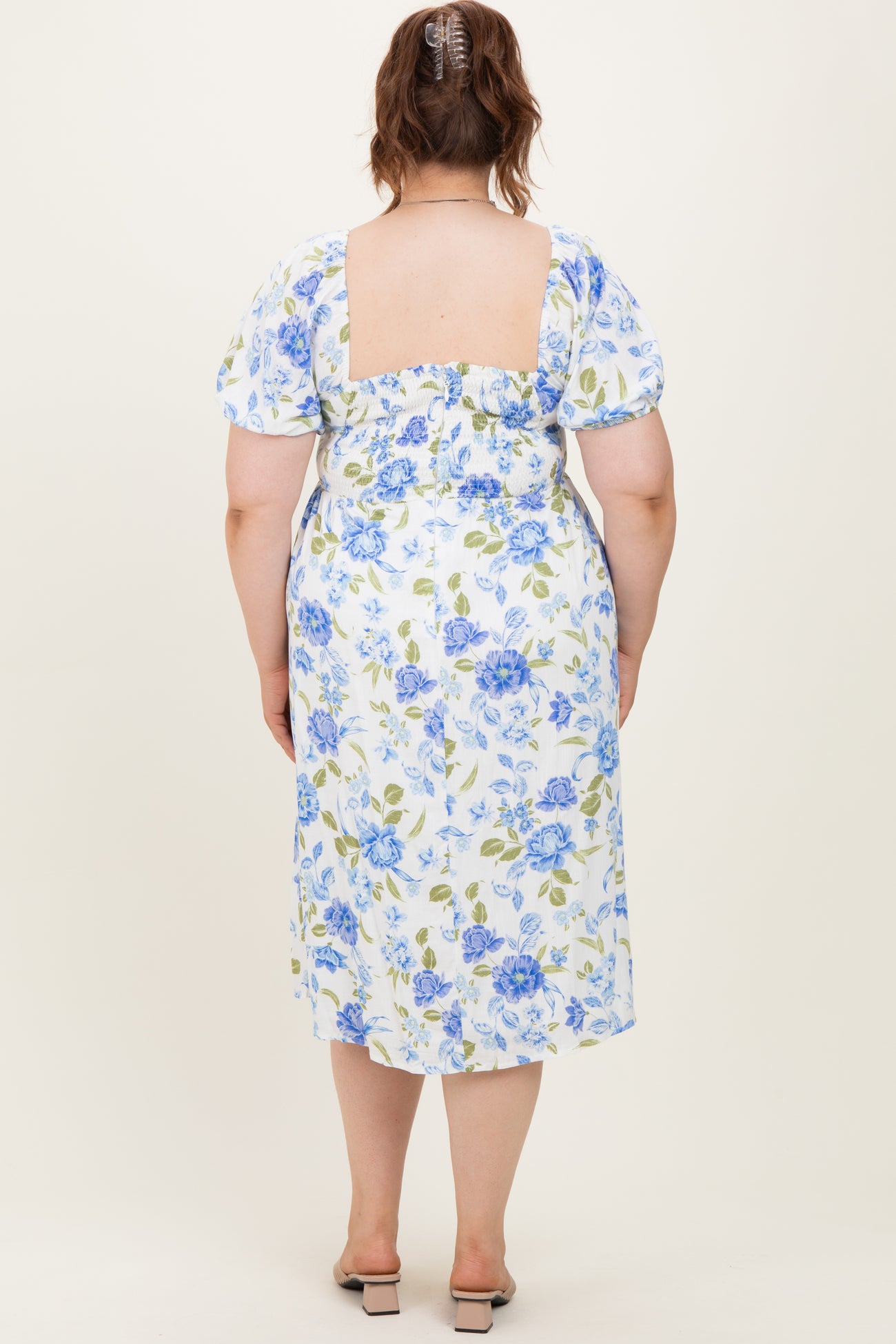 woman wearing a white floral maternity plus dress with blue and green flowers, showing a fitted back and puff sleeves