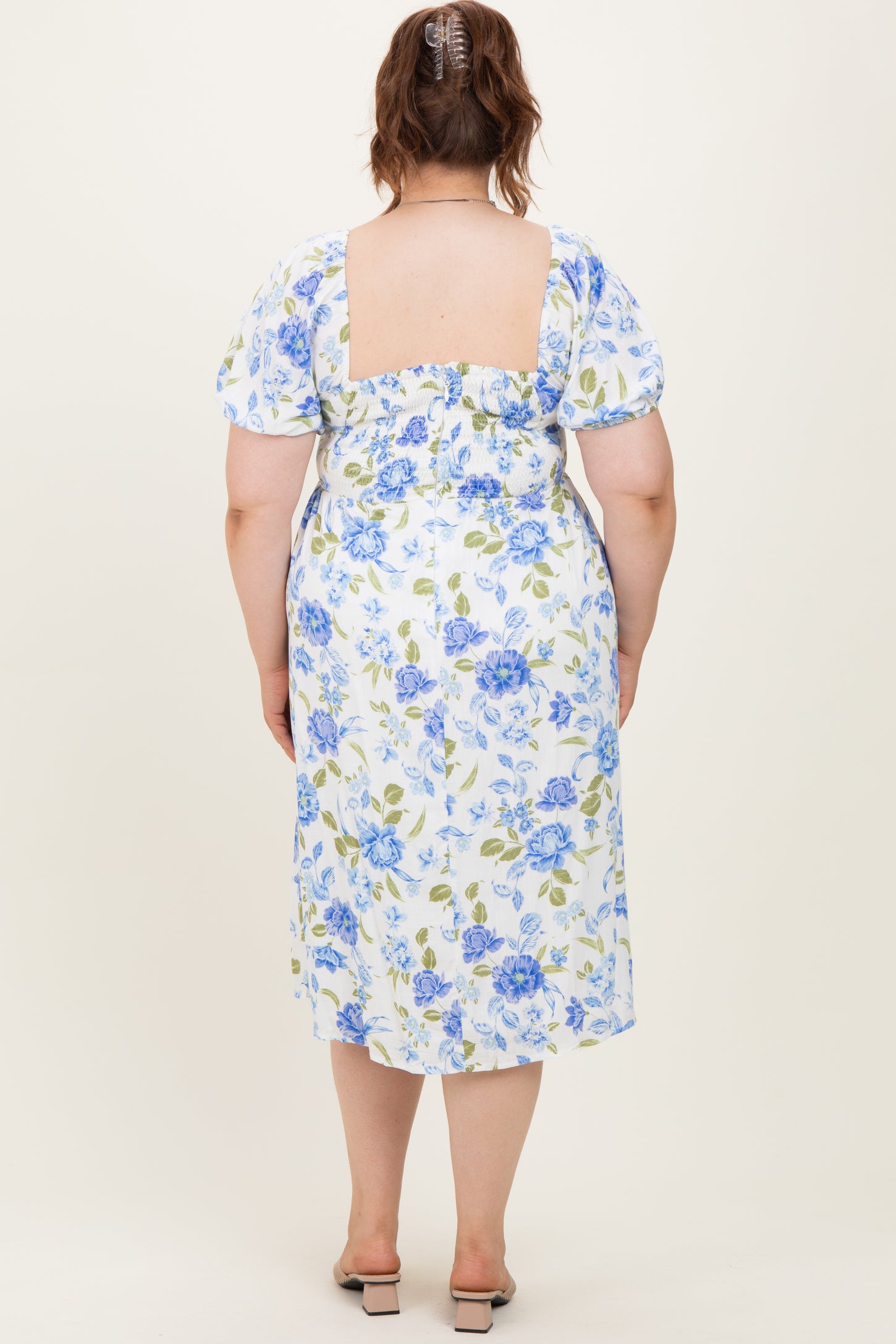 woman wearing a white floral maternity plus dress with blue and green flowers, showing a fitted back and puff sleeves