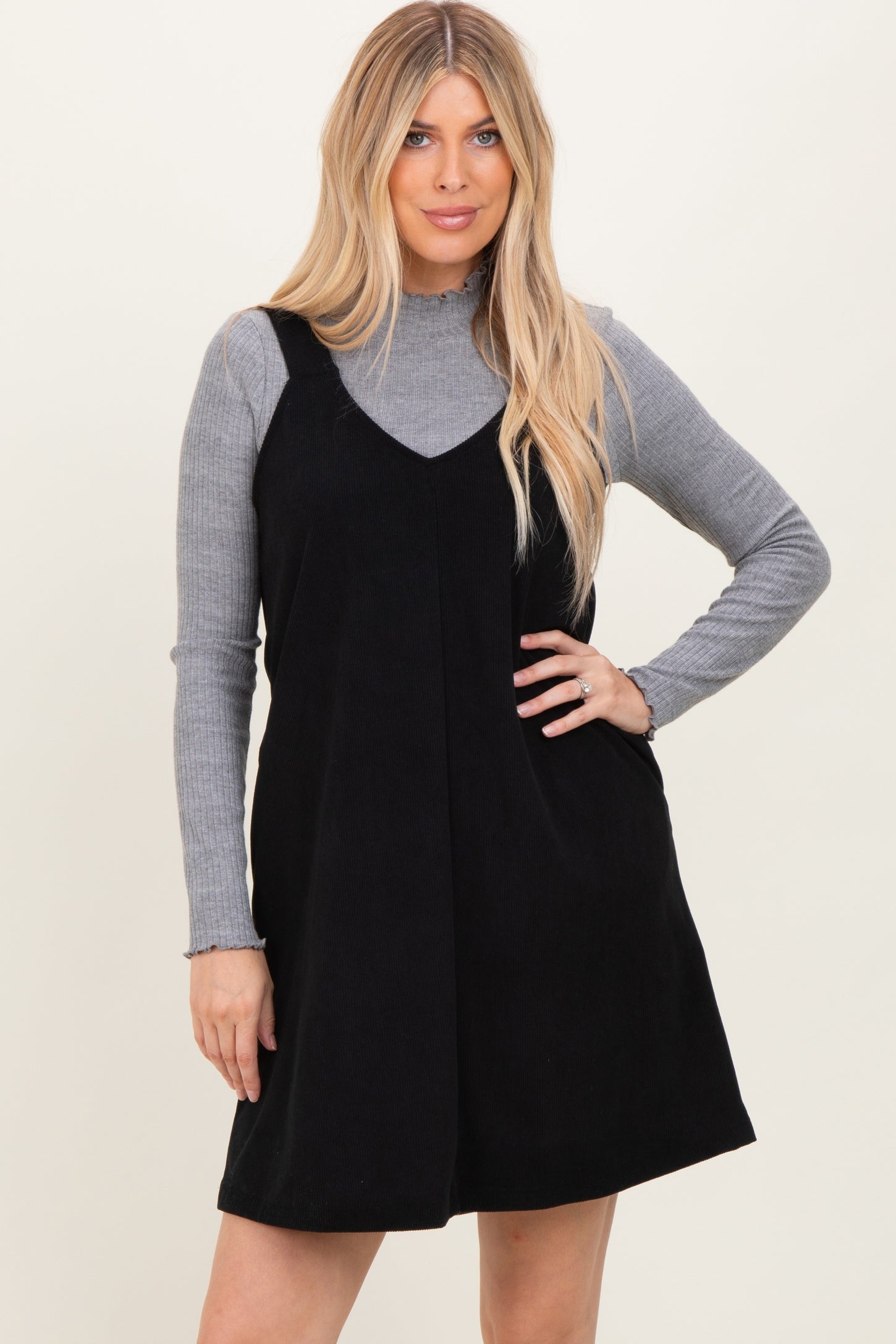 woman wearing a black corduroy overall dress over a gray long sleeve top