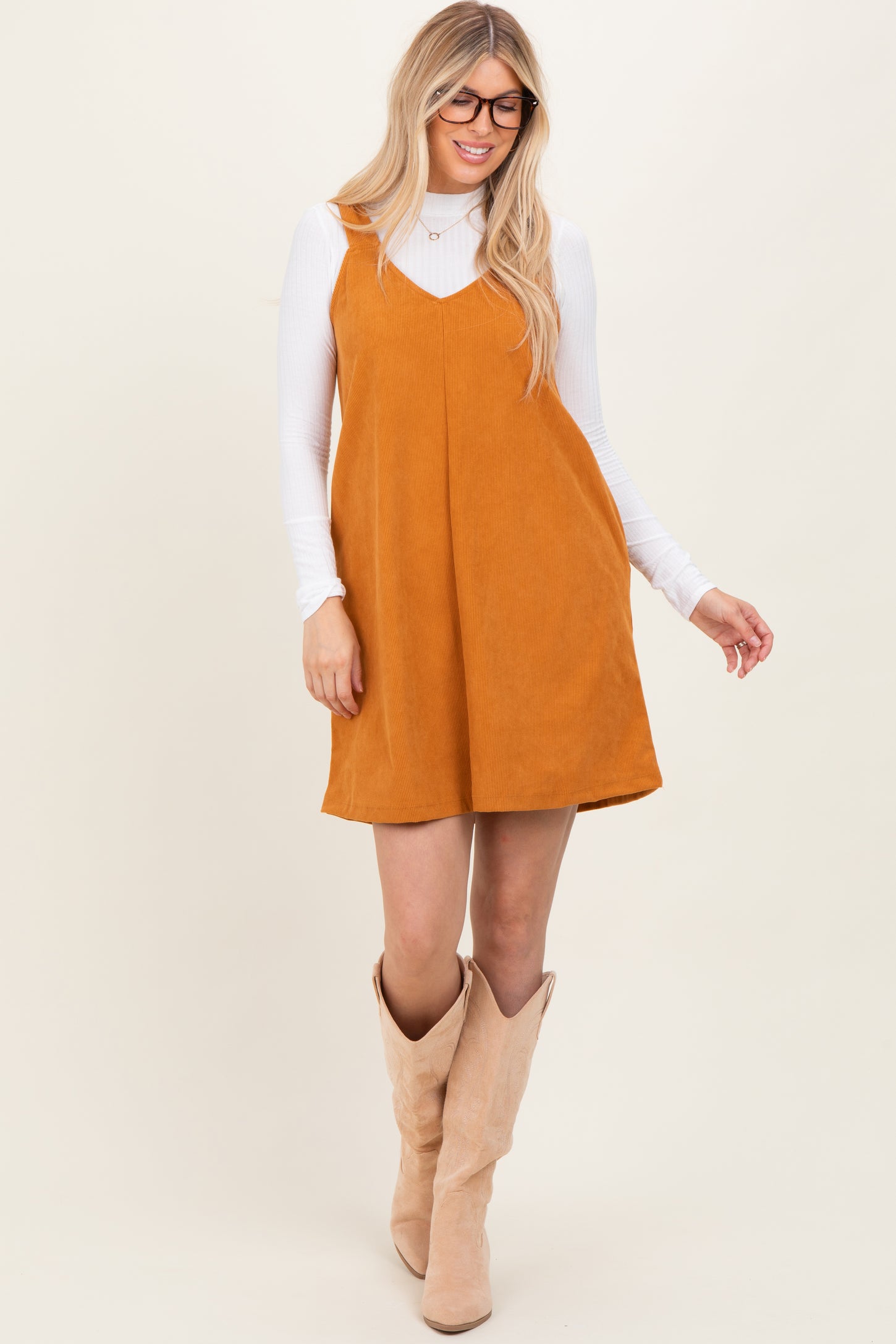 woman wearing a mustard corduroy overall dress over a white long sleeve top and tan knee-high boots