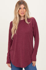 woman wearing a burgundy long sleeve ribbed top with a curved hem and relaxed fit