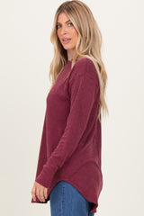 woman wearing a maroon long sleeve ribbed top with a high-low hem and side slits, styled with blue jeans