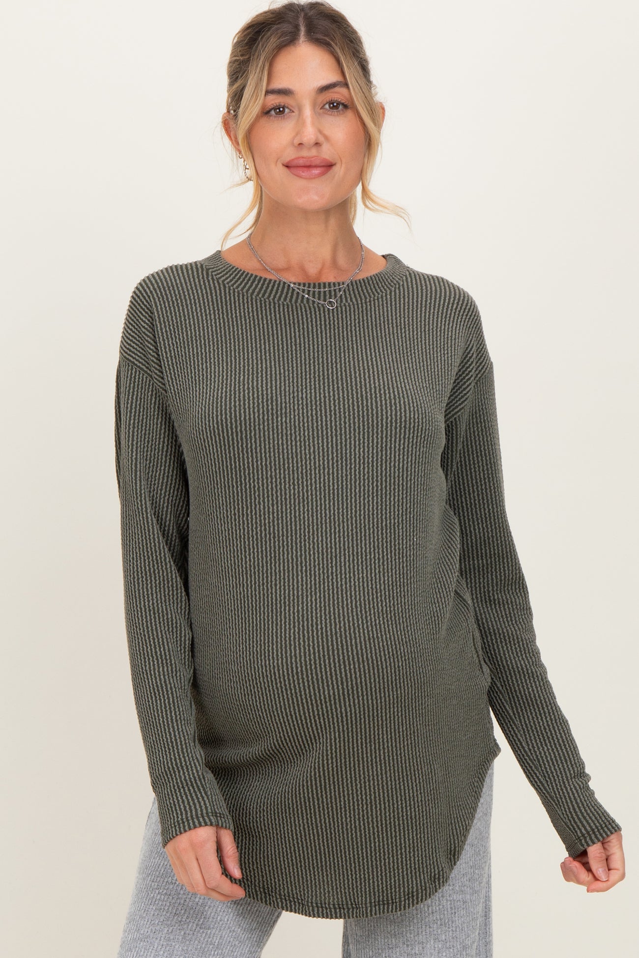 woman wearing a dark green ribbed maternity top with a rounded hem and long sleeves, showcasing her baby bump