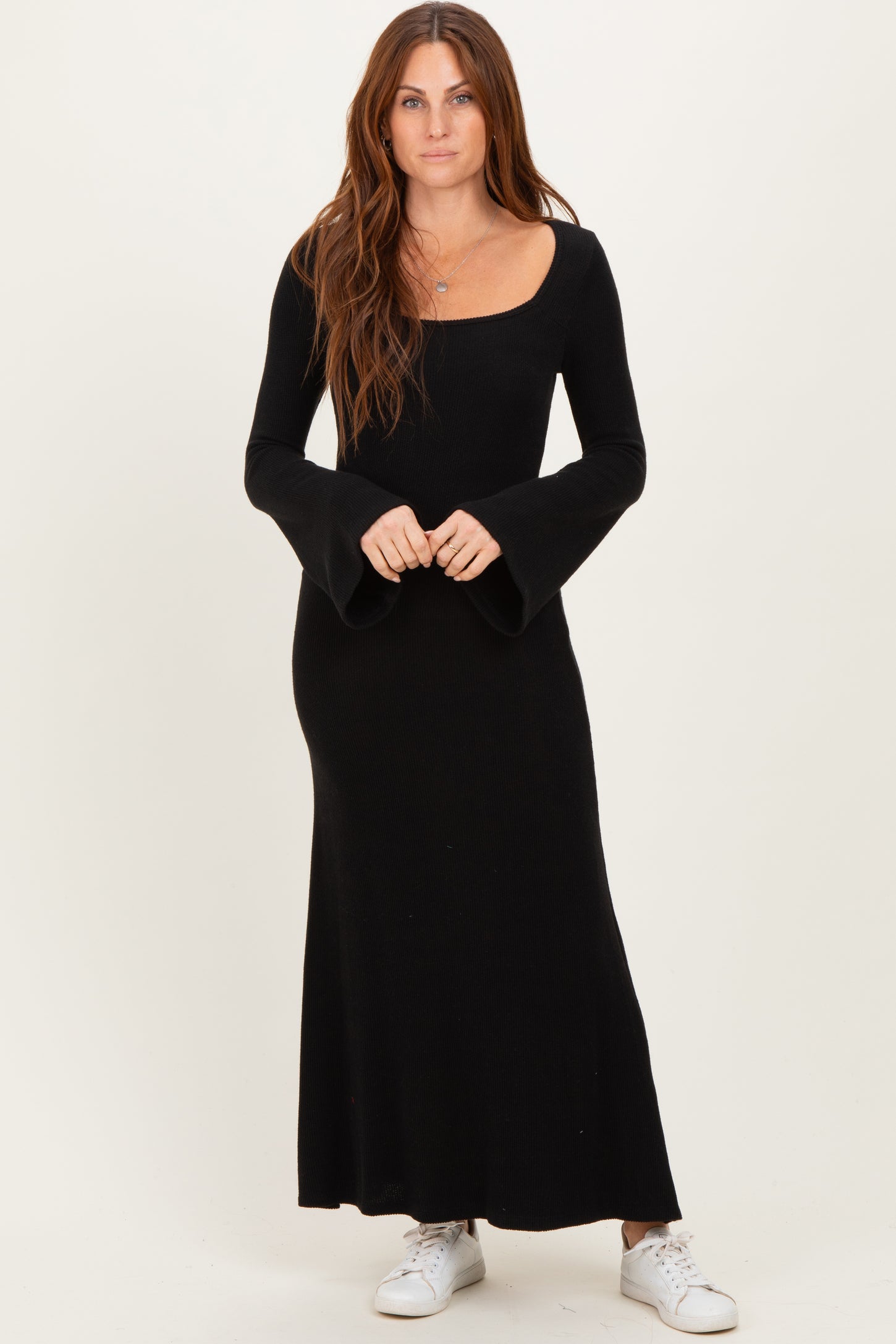 woman wearing a black long sleeve maxi dress with flared sleeves and a square neckline, styled with white sneakers