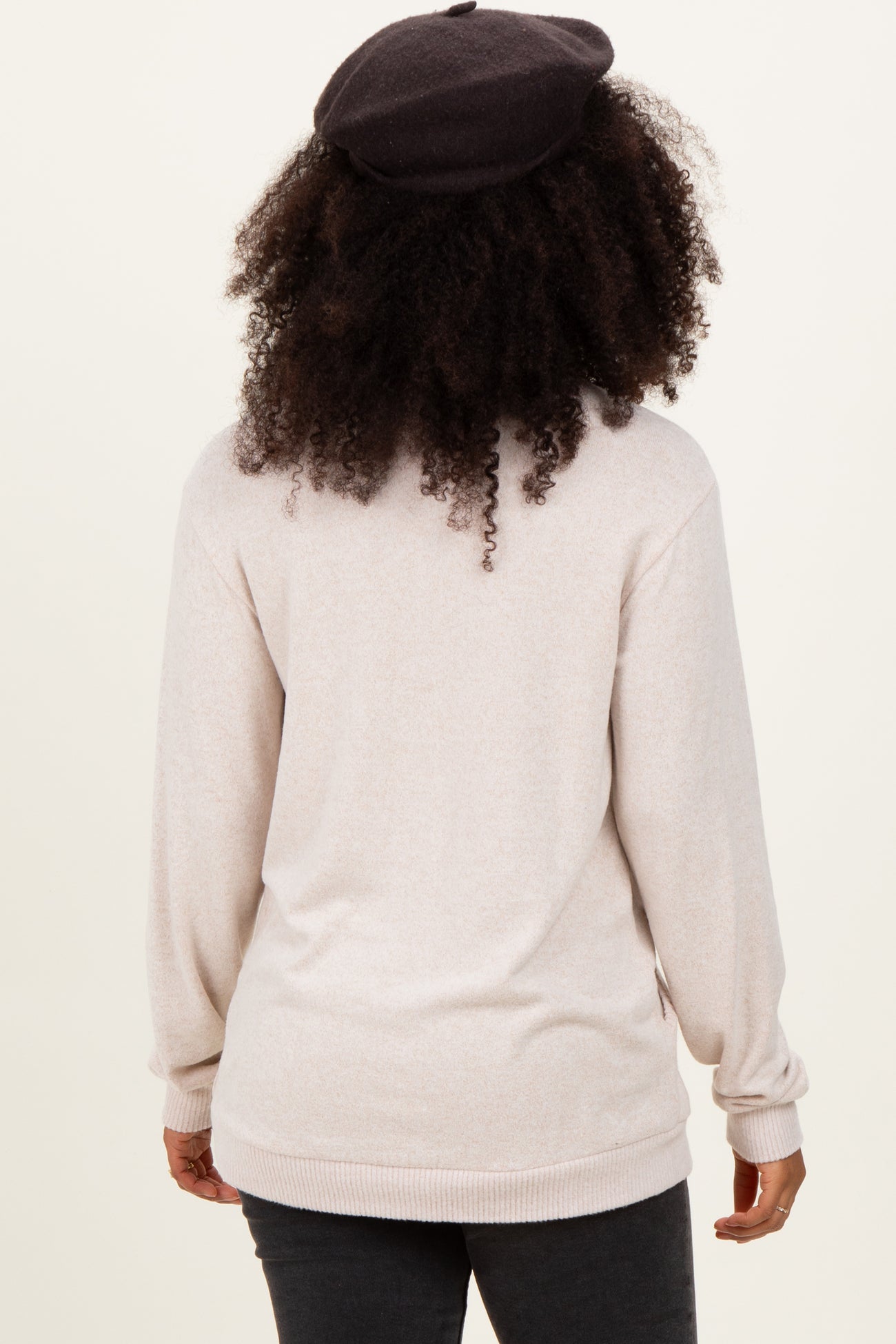 woman wearing a light beige long sleeve sweater, seen from the back, with curly hair and a black beret