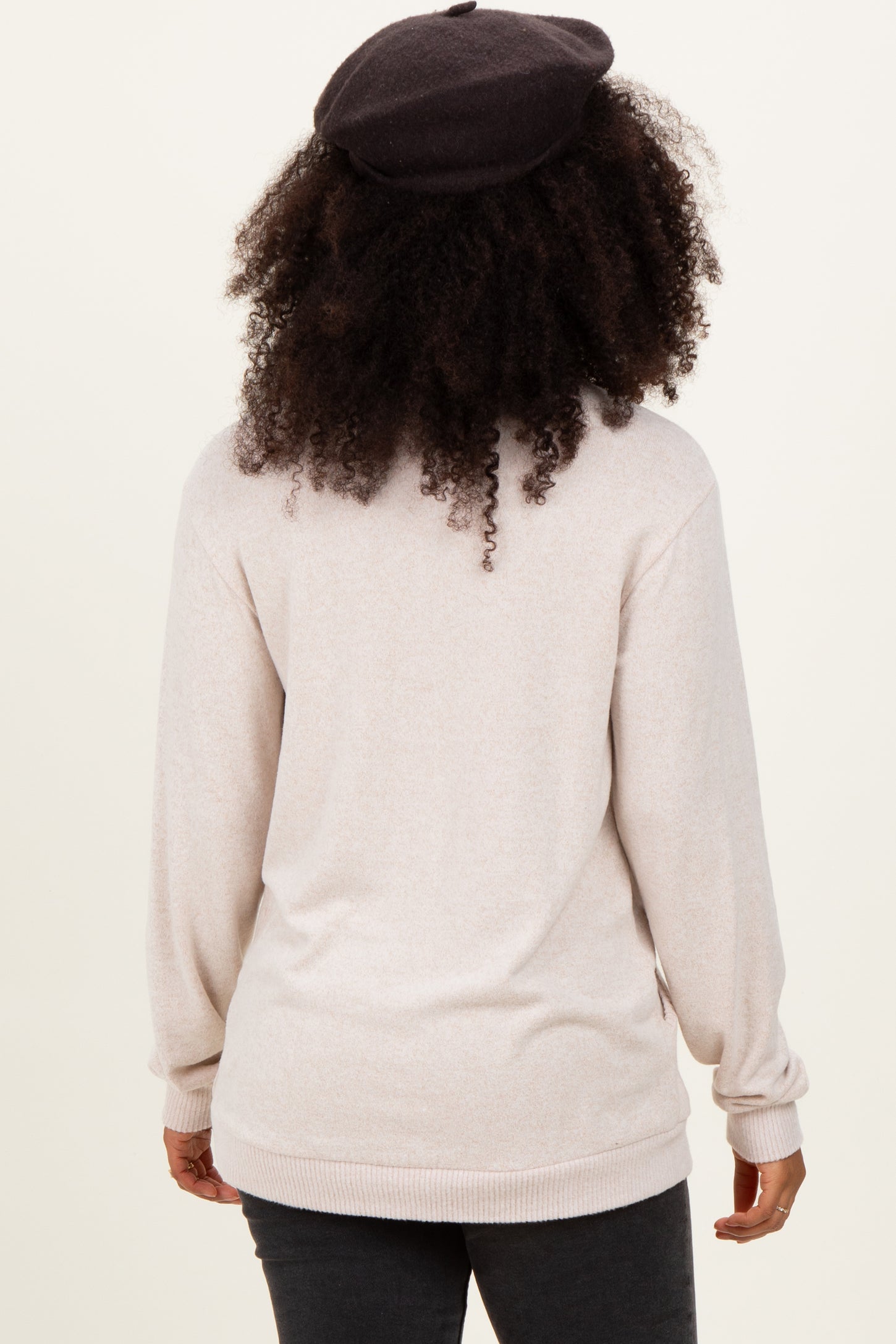woman wearing a light beige long sleeve sweater, seen from the back, with curly hair and a black beret