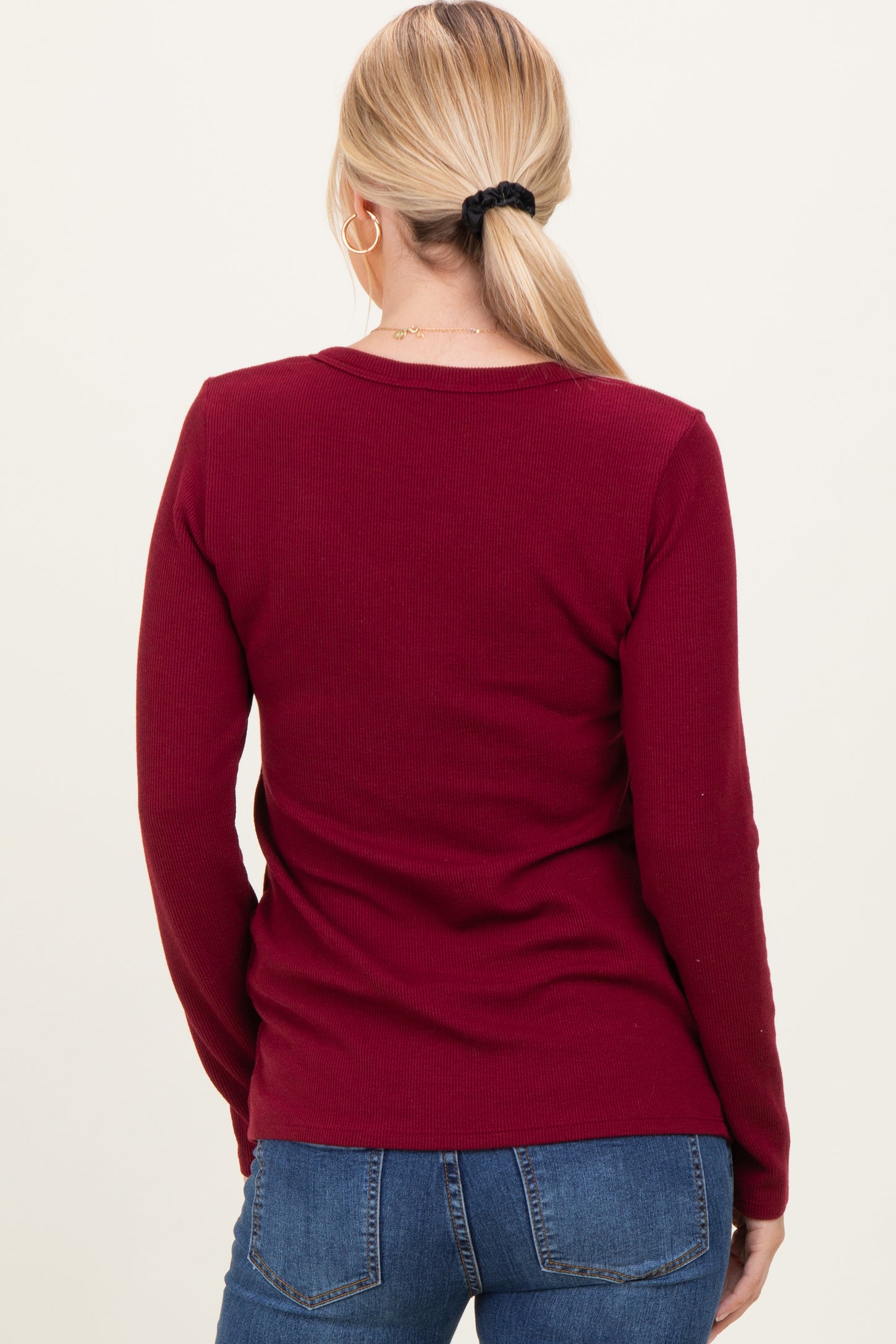 woman wearing a burgundy ribbed long sleeve top, viewed from the back, paired with blue jeans