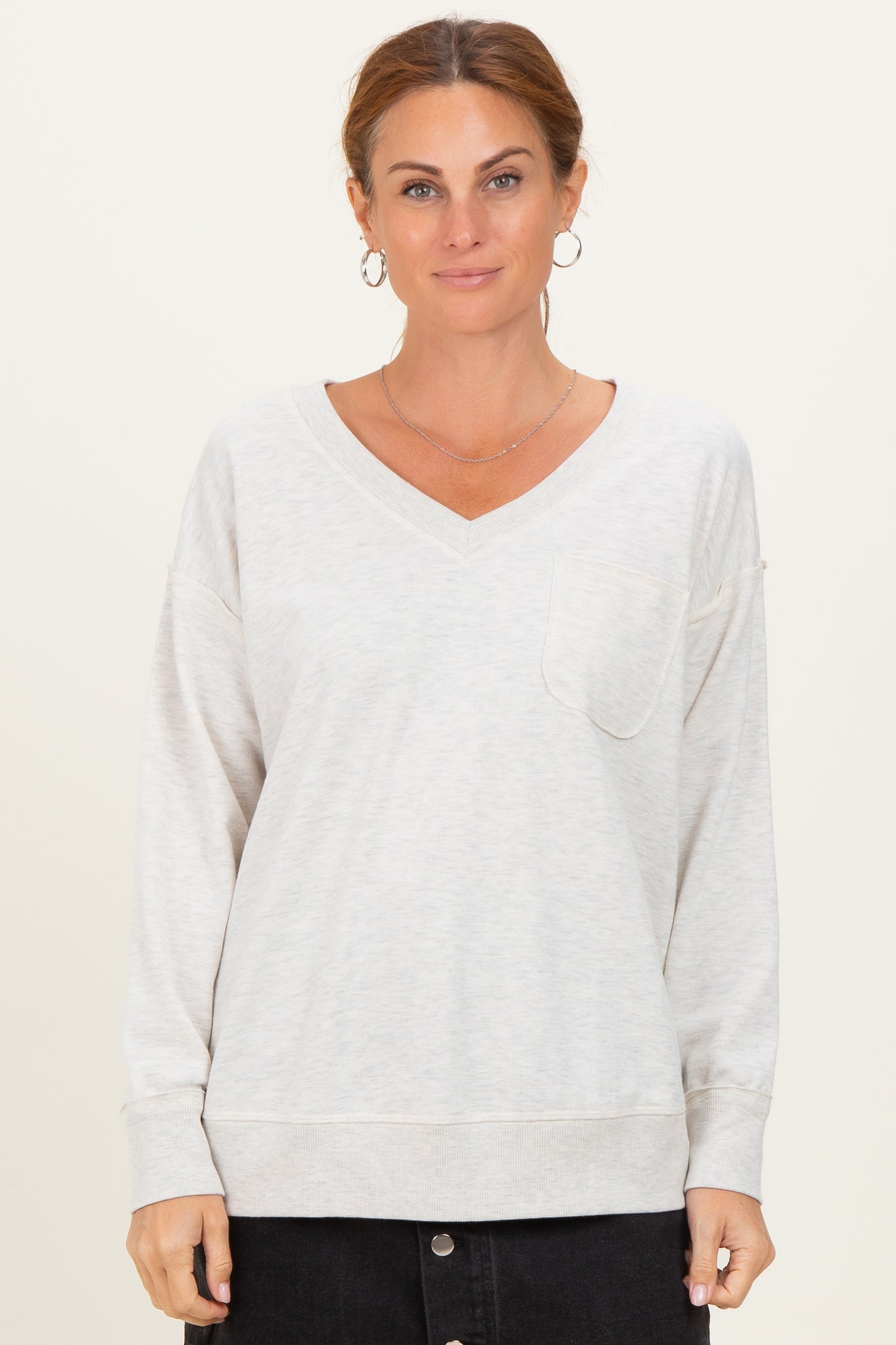 woman wearing a light gray v-neck long sleeve sweatshirt with a front pocket and relaxed fit