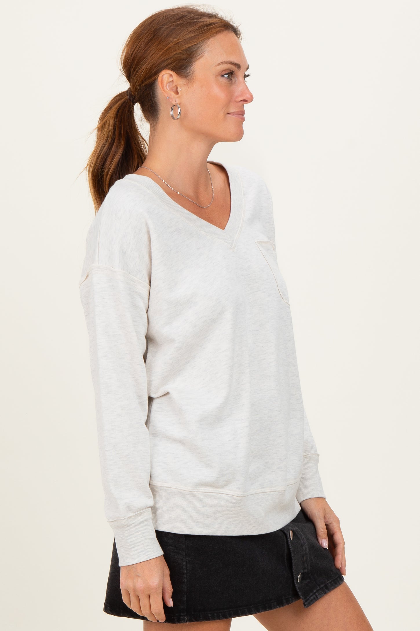 woman wearing a light gray v-neck sweatshirt with a pocket and black denim skirt