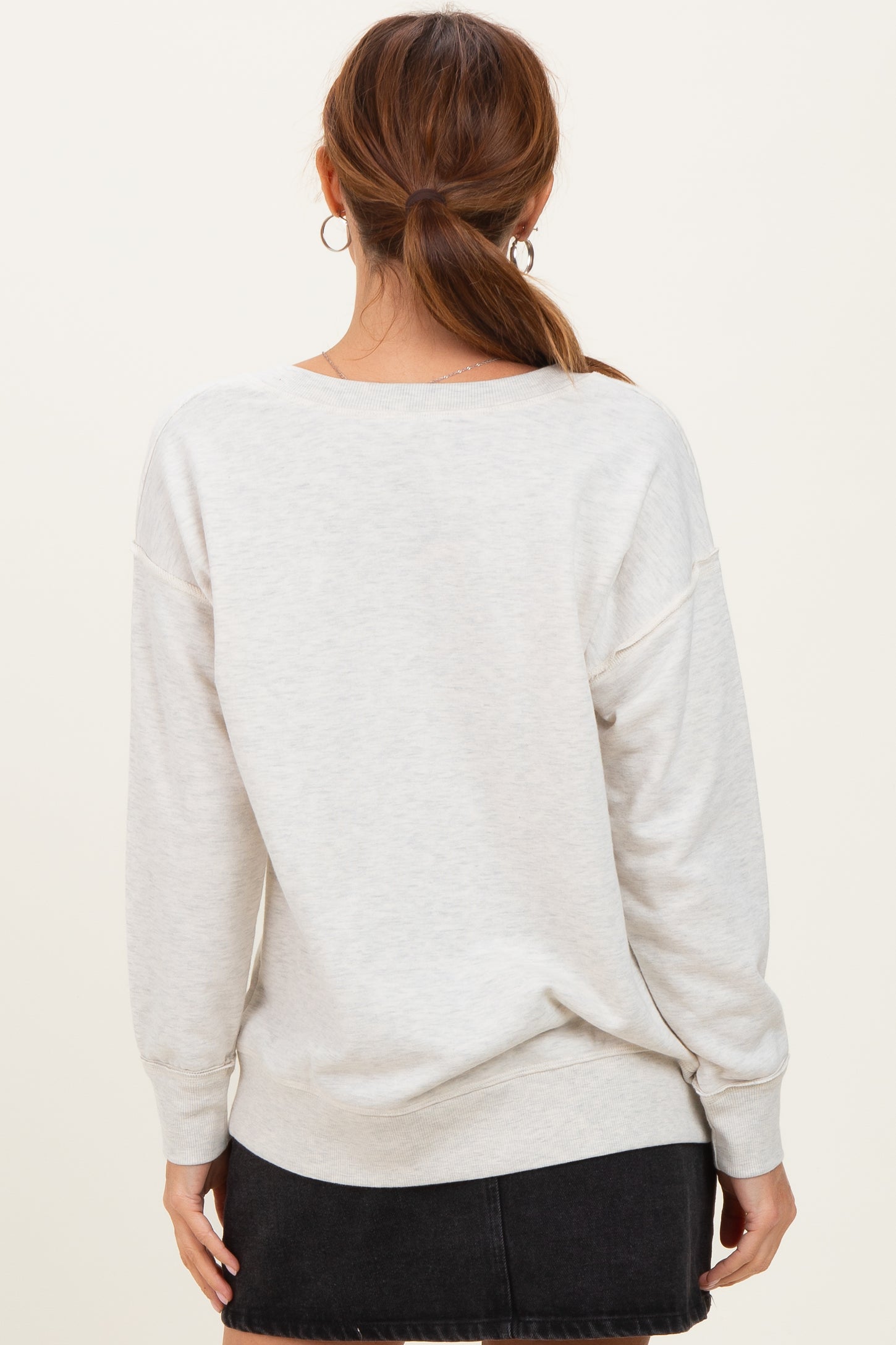 woman wearing a light gray oversized sweatshirt with drop shoulders and long sleeves, facing away from the camera