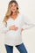 woman wearing a beige maternity sweatshirt with a v-neck and pocket, holding her baby bump