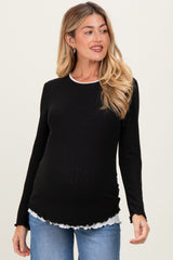 woman wearing a black maternity long sleeve top with a white ruffled hem and a visible baby bump
