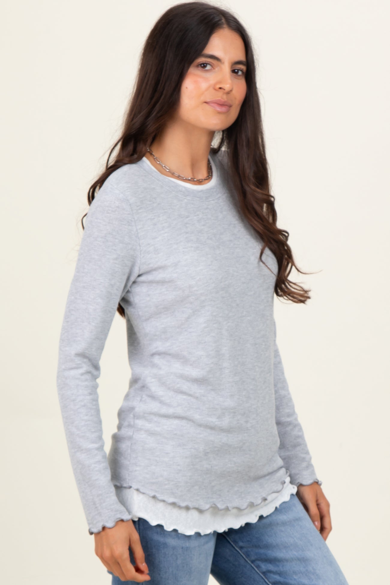 woman wearing a light gray long sleeve top with scalloped hem and casual jeans