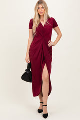 woman wearing a burgundy short sleeve maxi dress with a twist detail and thigh-high slit, holding a black handbag
