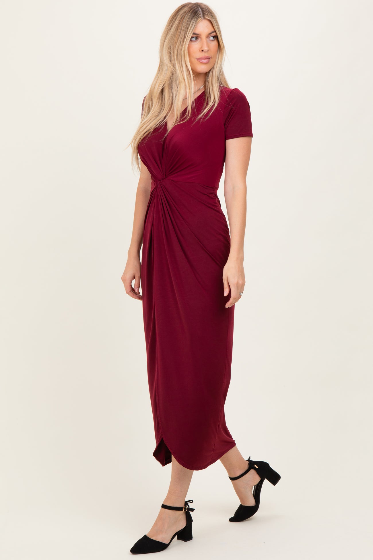 woman wearing a burgundy short sleeve midi dress with a knotted front detail and black ankle strap heels