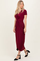 woman wearing a burgundy short sleeve midi dress with a knotted front detail and black ankle strap heels