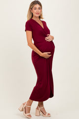 woman wearing a burgundy maternity dress with short sleeves and a wrap detail, holding her baby bump