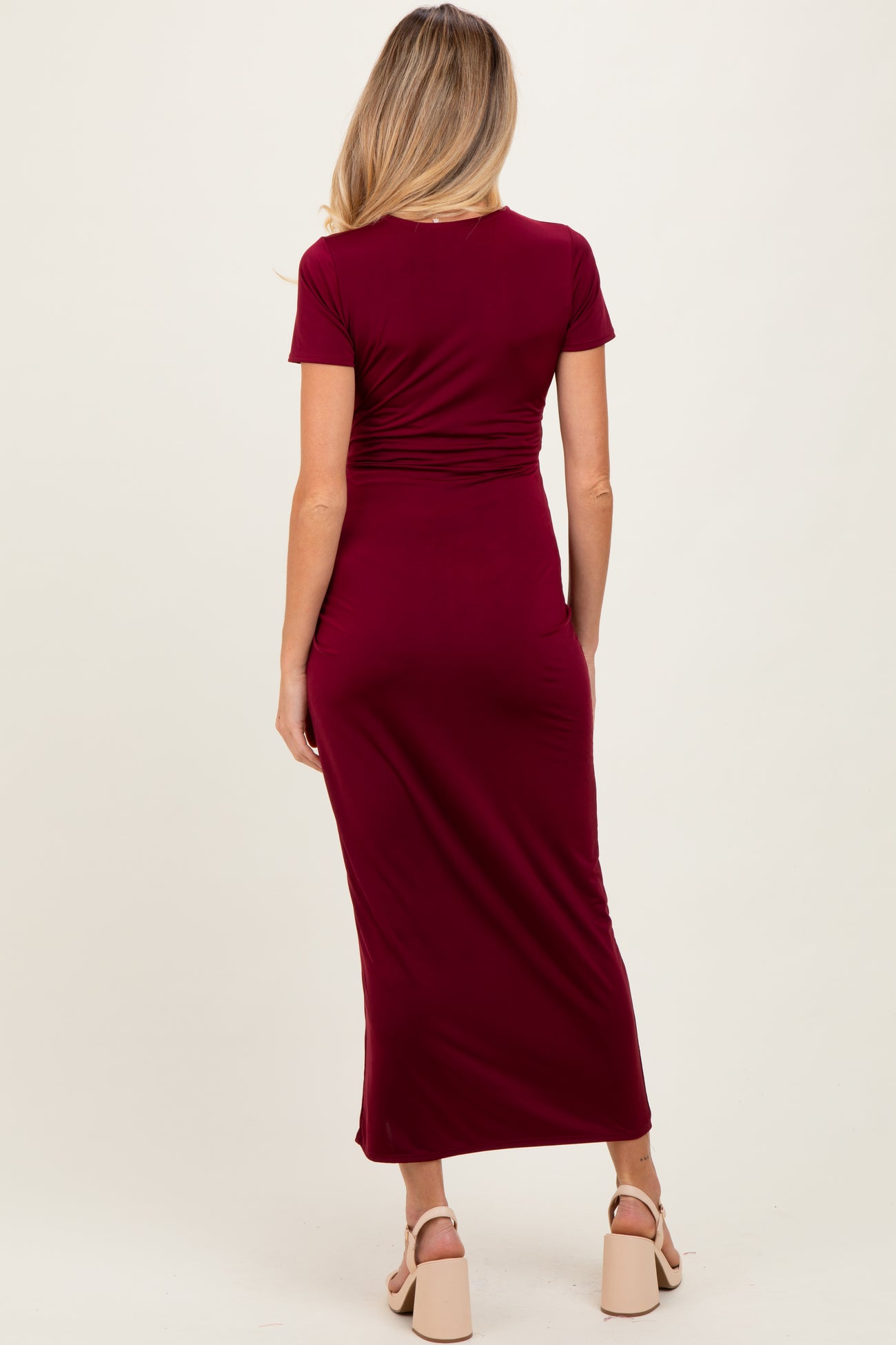 woman wearing a burgundy short sleeve maternity dress, showing a fitted silhouette and mid-length skirt from the back