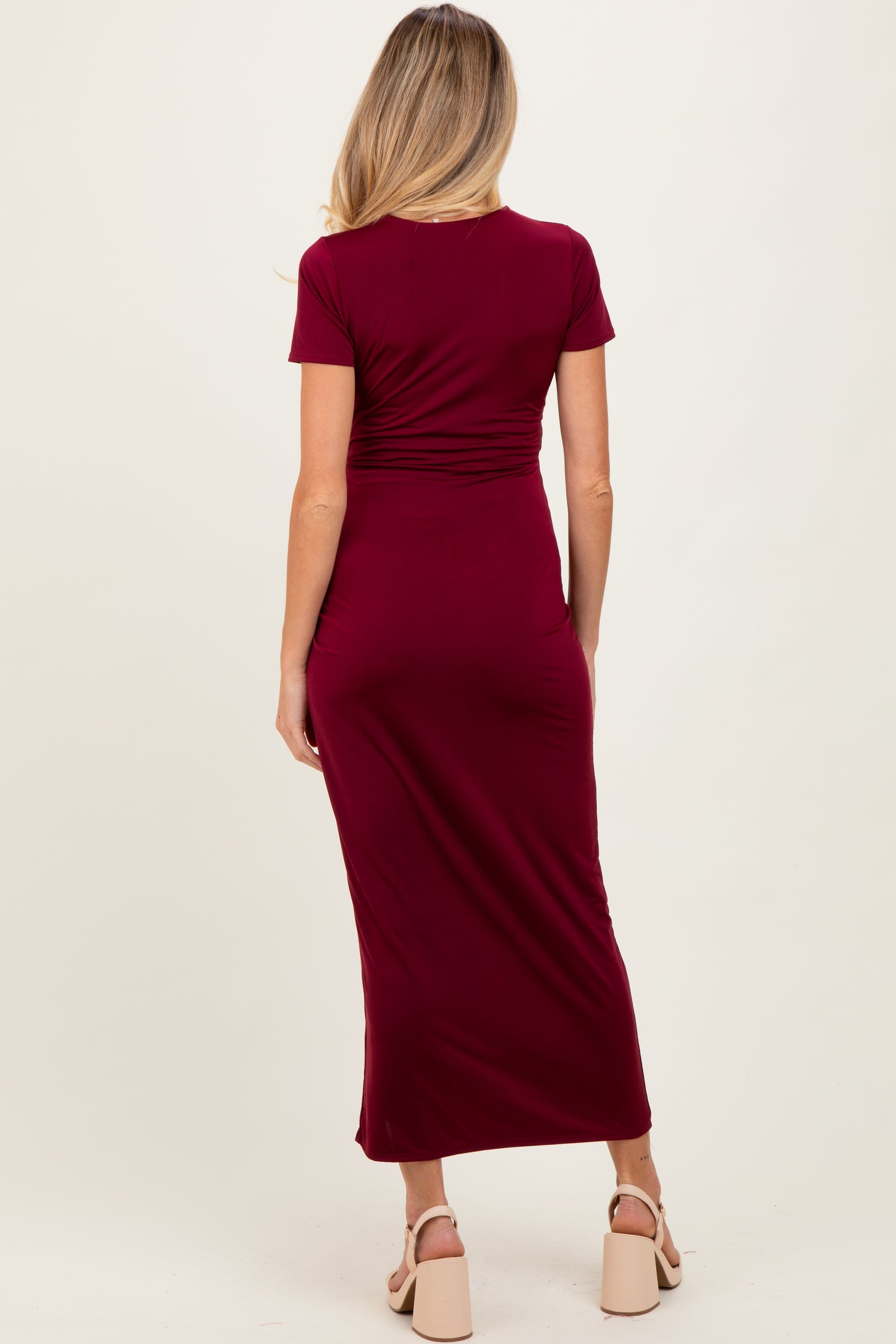 woman wearing a burgundy short sleeve maternity dress, showing a fitted silhouette and mid-length skirt from the back