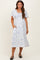woman wearing a white floral print maternity dress with short sleeves and pockets, standing against a neutral background