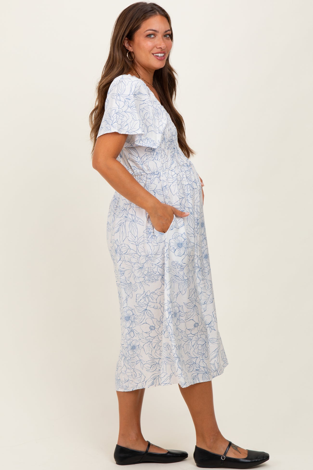 woman wearing a white maternity dress with blue floral print and pockets, showcasing her baby bump