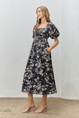 woman wearing a black floral puff sleeve midi dress with a square neckline and pockets