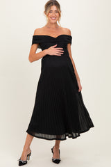 woman wearing a black off-the-shoulder maternity dress with pleated detail and holding her baby bump