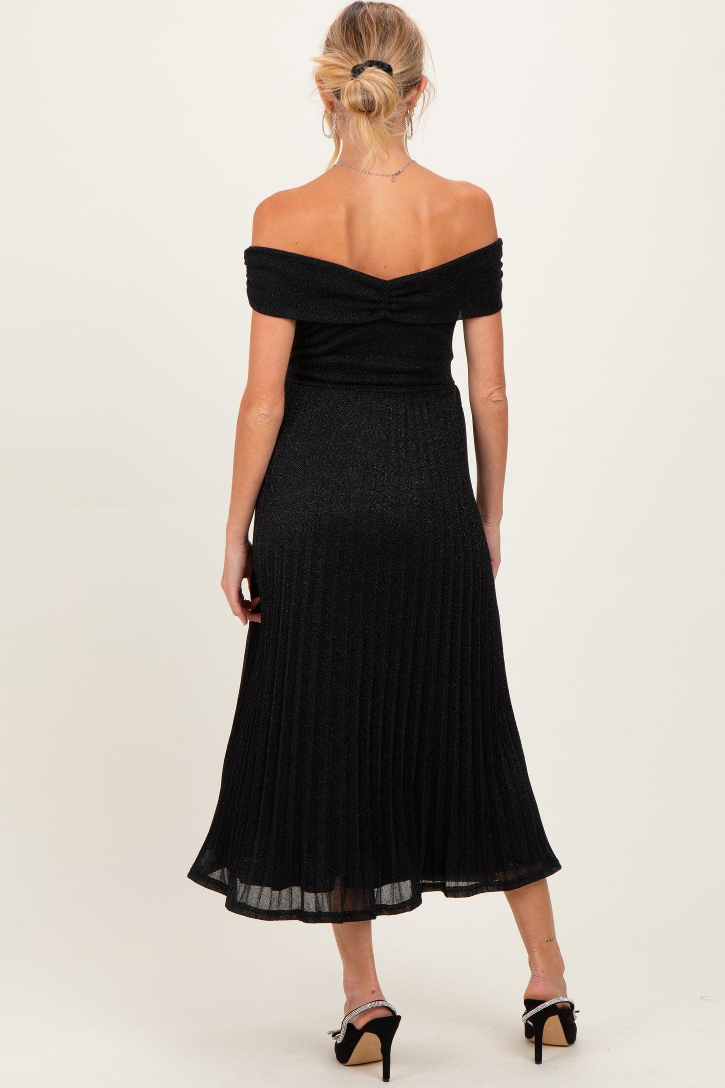 woman wearing a black off-the-shoulder maternity dress with a pleated skirt, showing a sleek back view
