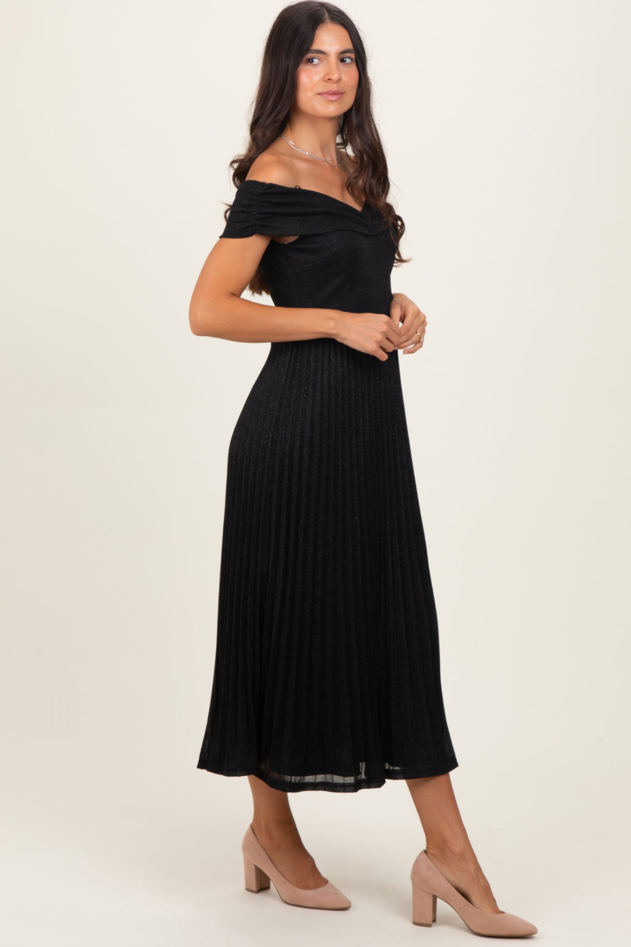 woman wearing a black off-the-shoulder pleated midi dress and nude heels