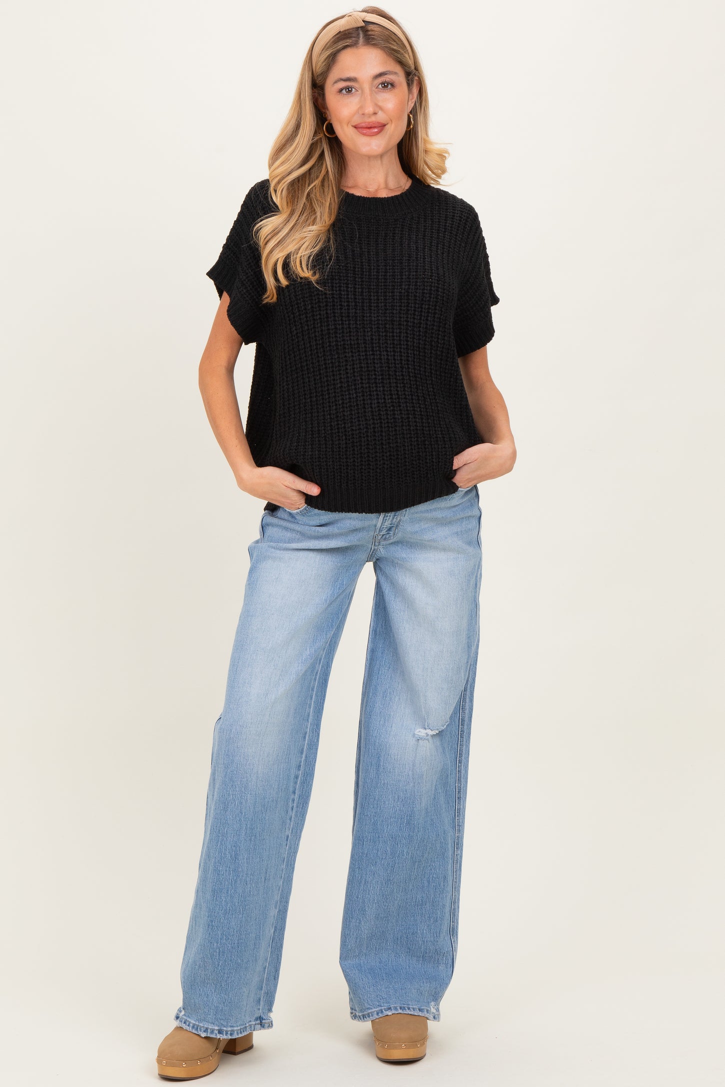 woman wearing a black knitted maternity sweater and light blue wide-leg jeans, with a relaxed fit and casual style