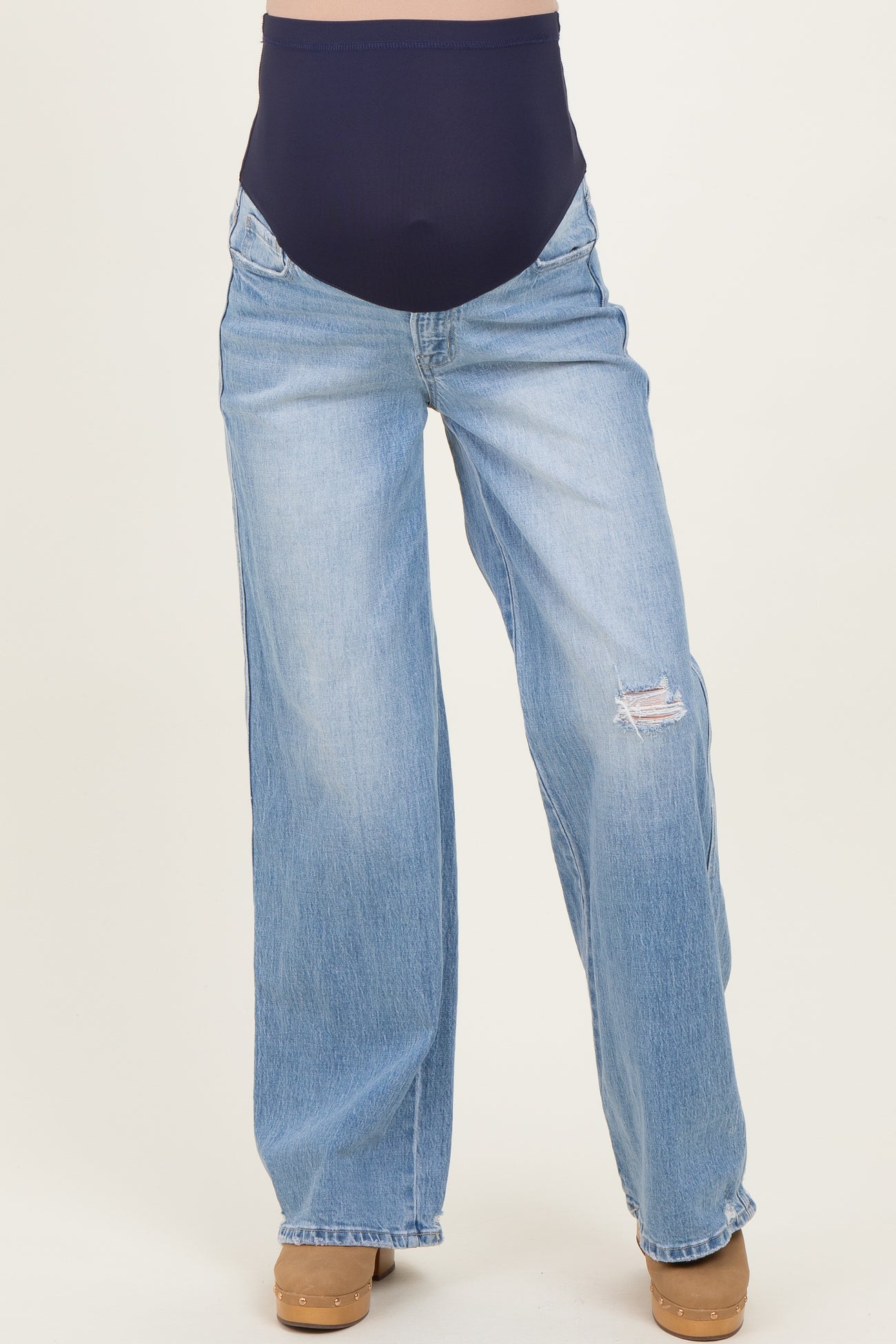 woman wearing a pair of light blue distressed maternity jeans with a navy blue over-the-bump panel